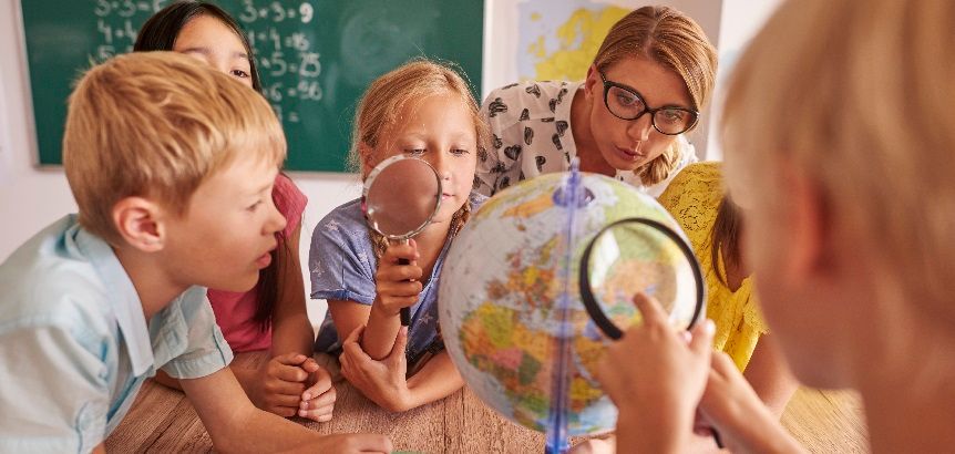 A classroom scene of children discovering new places on a globe together.